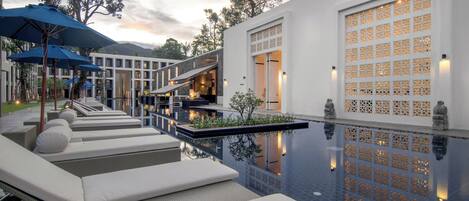 A modern hotel with a swimming pool, lounge chairs, and a decorative wall with a lattice design.