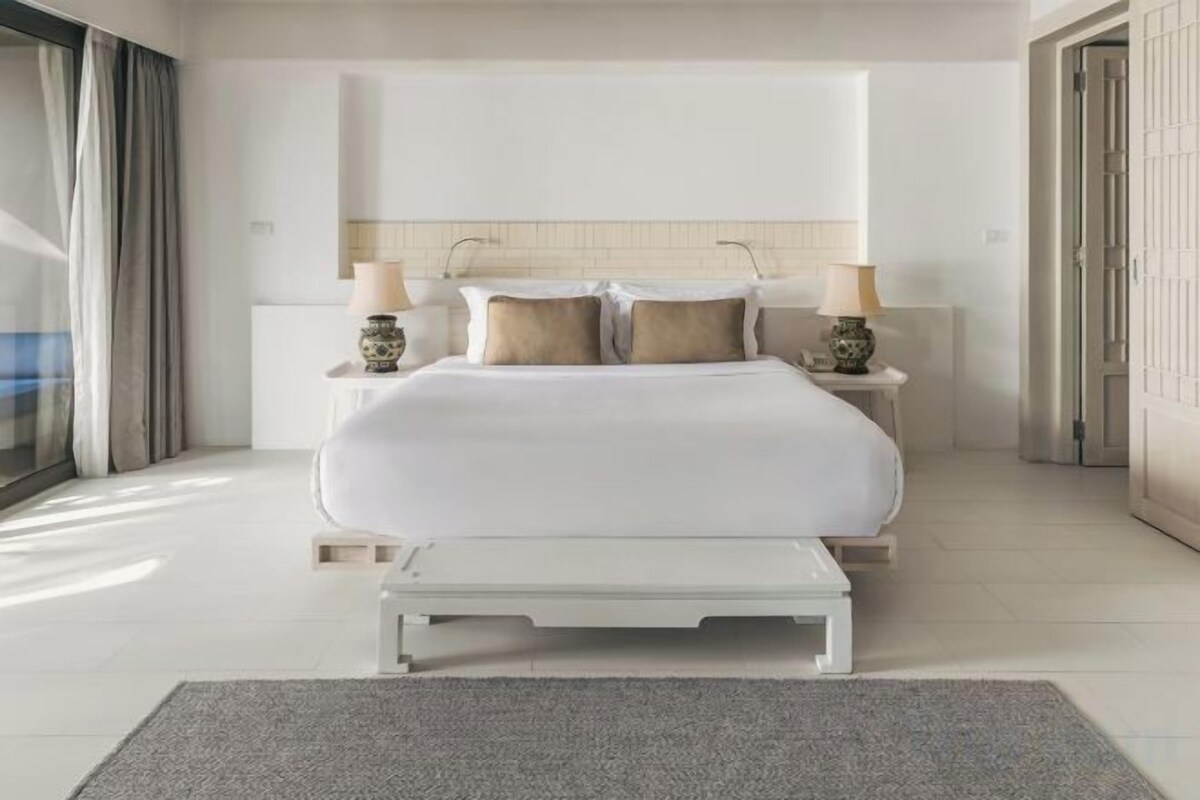 Ein modernes Schlafzimmer mit einem großen Bett, Nachttischen und Blick ins Freie.