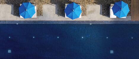 Área de piscina no terraço com três guarda-sóis azuis e um caminho de azulejos.