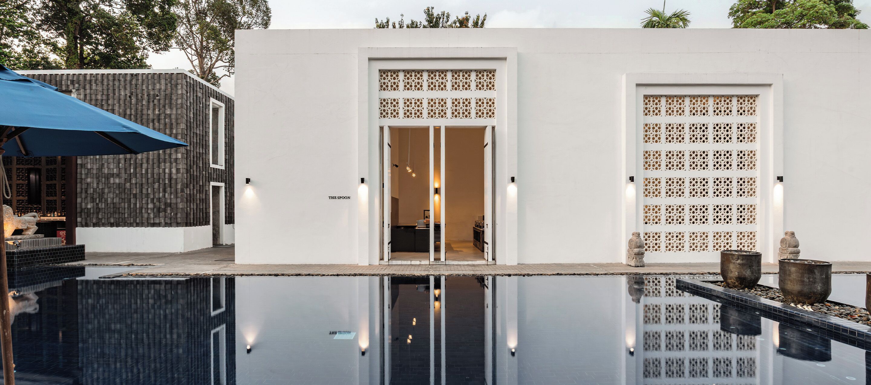 A modern building with a pool, a blue umbrella, and a decorative fence.