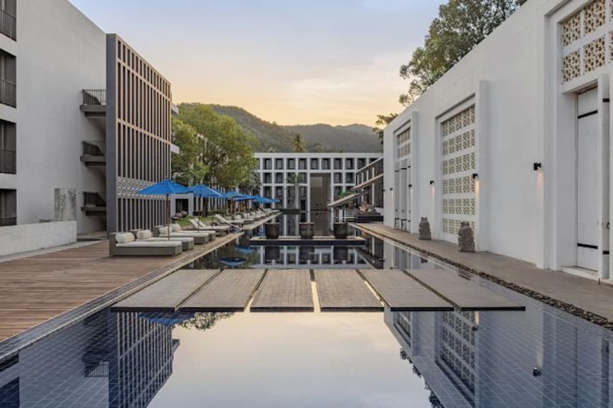 A modern hotel with a pool, outdoor seating, and a view of the mountains.