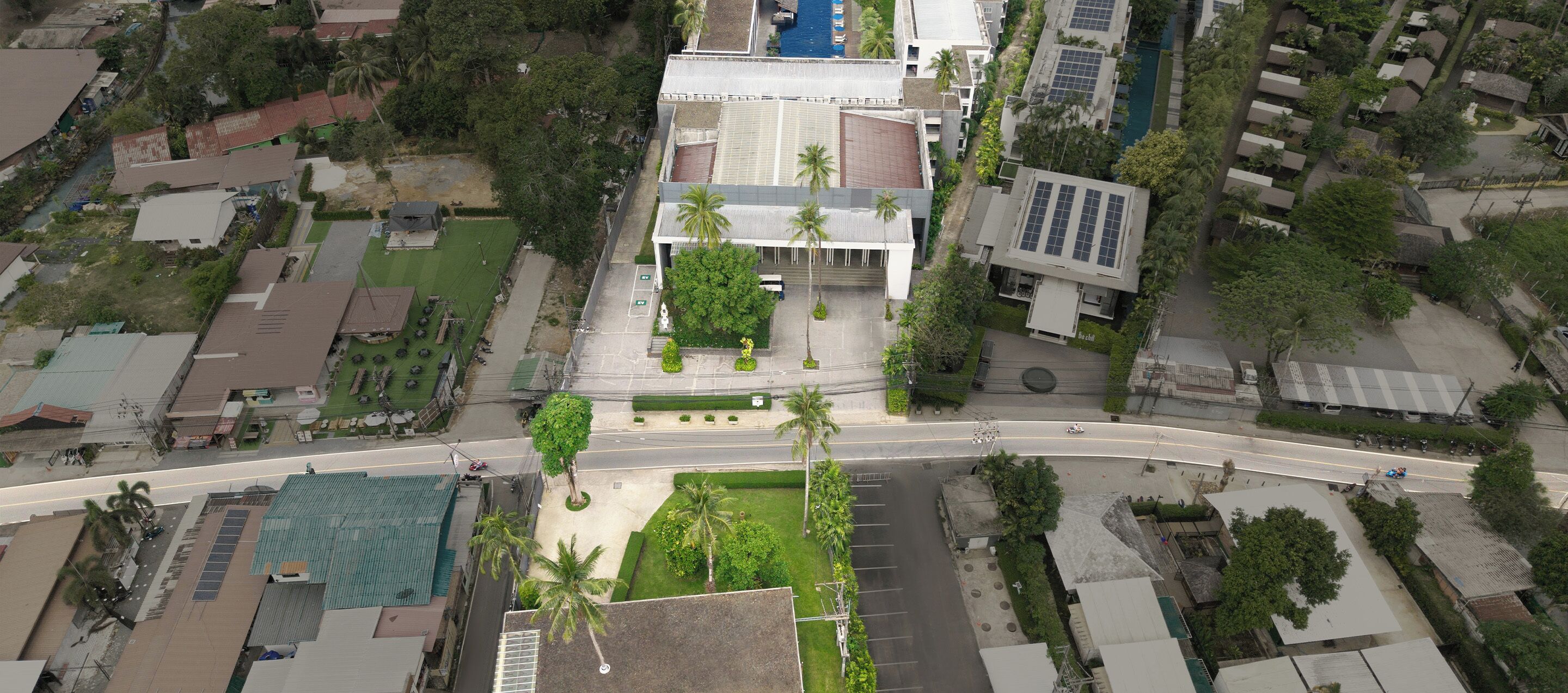 An aerial view of a residential area with a prominent building featuring a flat roof, a swimming pool, and a parking lot.