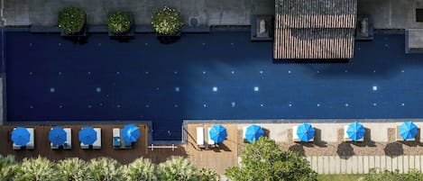 Vista aérea de una zona de piscina en la azotea con múltiples sillones de descanso y sombrillas, rodeada de vegetación y una terraza de madera.