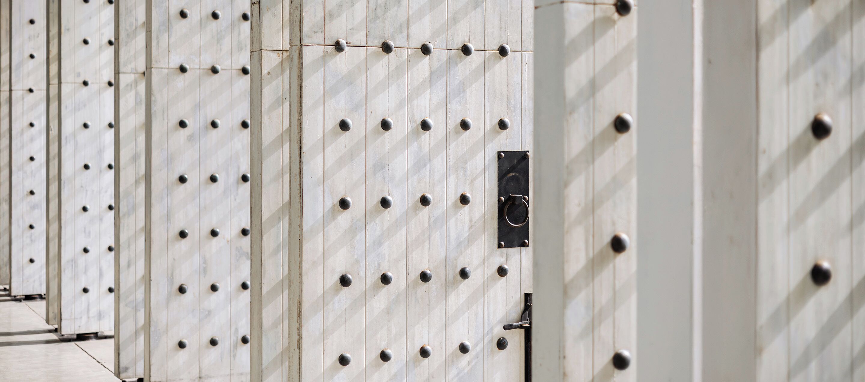 A row of white, industrial-style doors with evenly spaced round knobs and a black sign on one door.