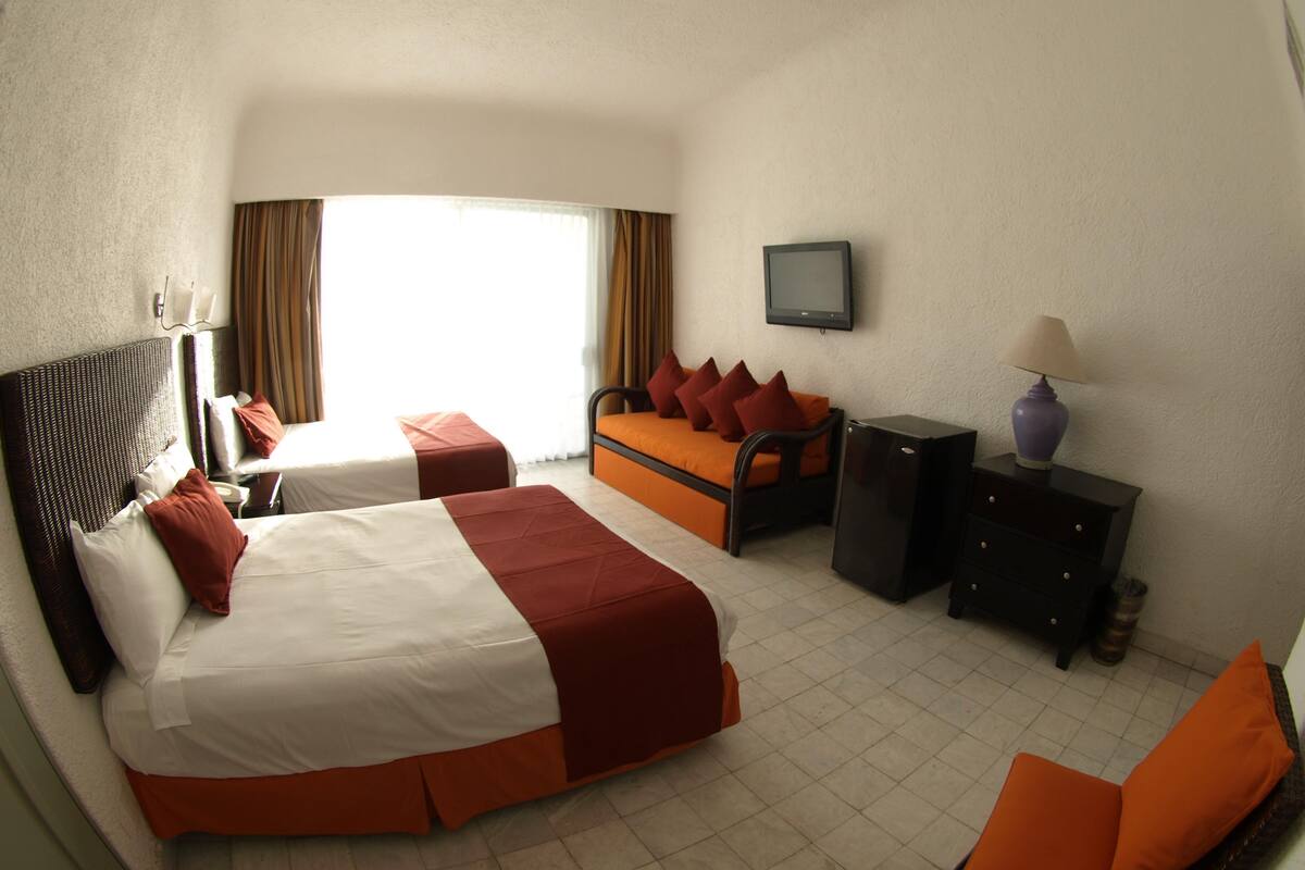 Habitación de hotel con dos camas, un sofá, un televisor y un escritorio con lámpara.
