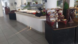 A buffet area with a variety of food items and a fan. There are potted plants and a sign indicating a bar area. - Sierra Mar Mazanillo (Manzanillo)