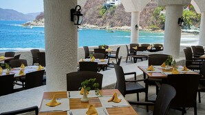 An outdoor dining area with tables and chairs, a view of the sea, and a mountainous backdrop. - Sierra Mar Mazanillo (Manzanillo)