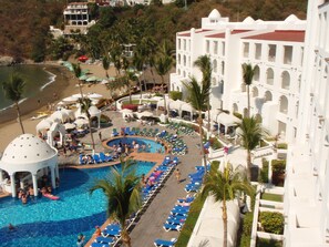 A resort with a central pool, sun loungers, and a beach area.