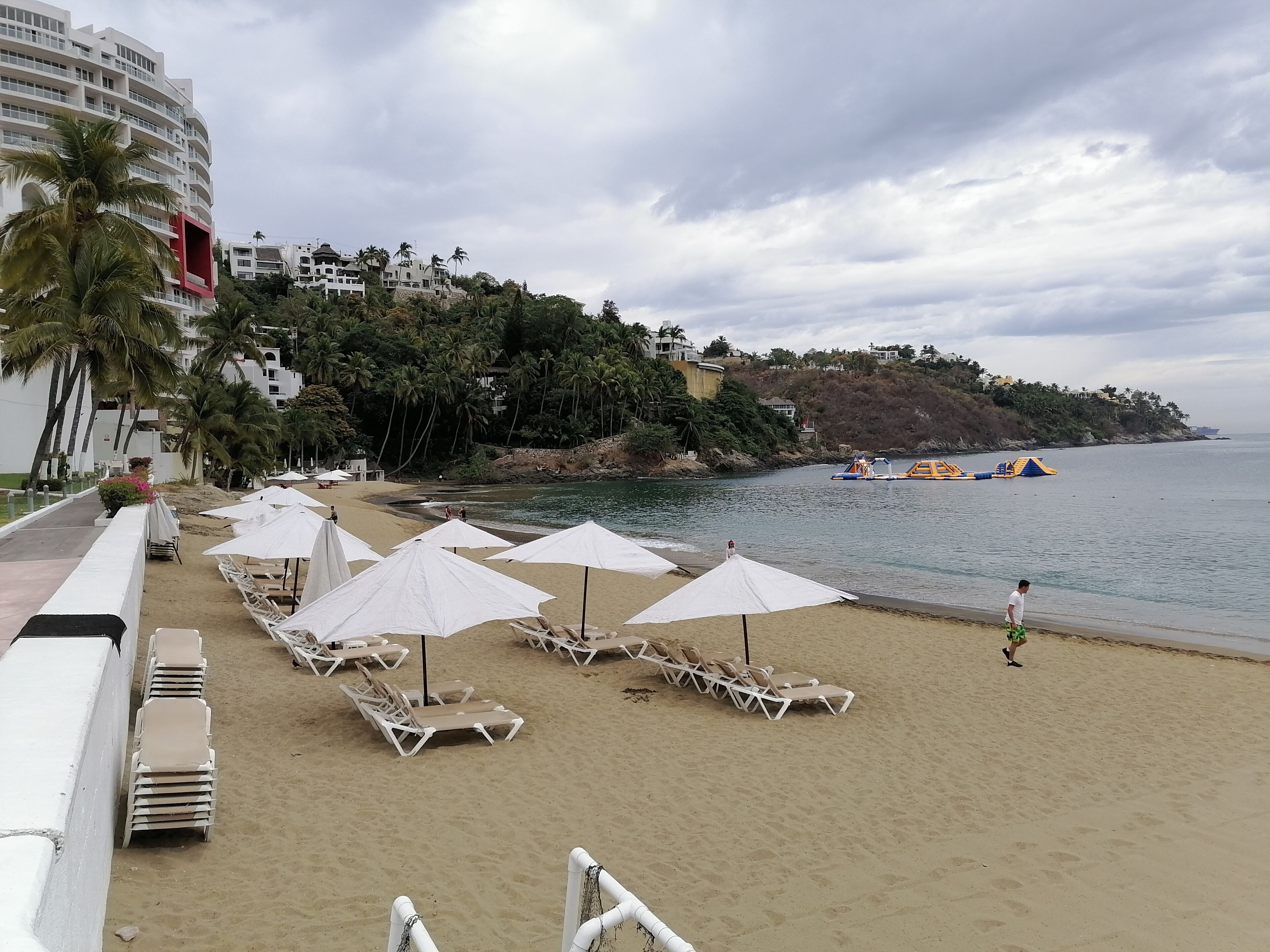 A beach with white umbrellas and lounge chairs, a sandy shore, and a building with balconies overlooking the sea.