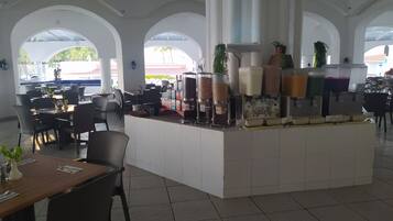 Un espacio de cafetería amplio y luminoso, con una barra central, diversas opciones de asientos y grandes ventanales.