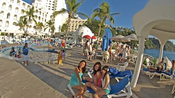 Zona de piscina en un resort con tumbonas, palmeras y vista al mar.