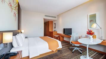 A hotel room with a bed, desk, chair, TV, lamp, and a vase with flowers.
