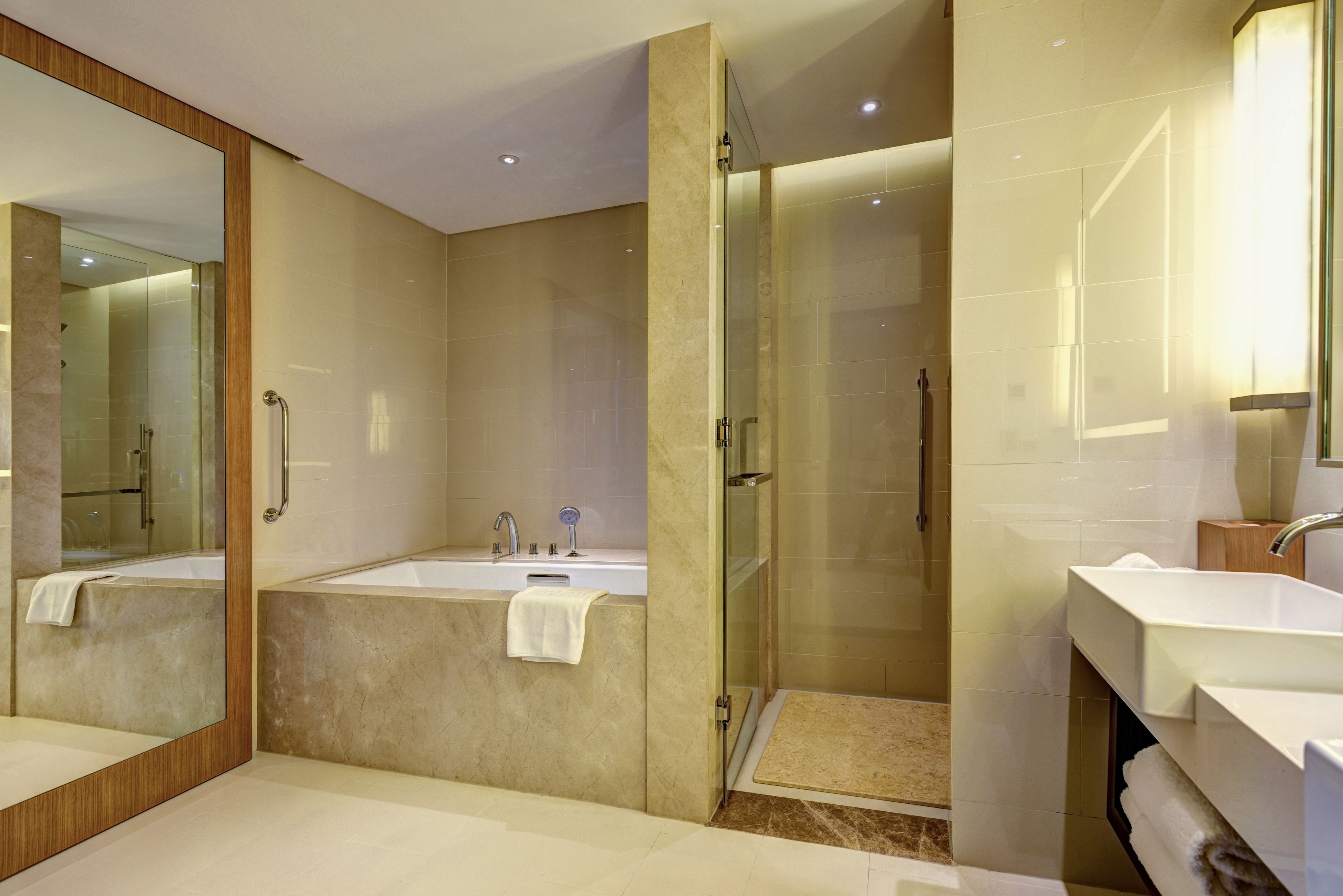 Une salle de bain moderne dotée d’un grand miroir, d’une baignoire, d’une zone de douche et d’un meuble-lavabo avec un évier.