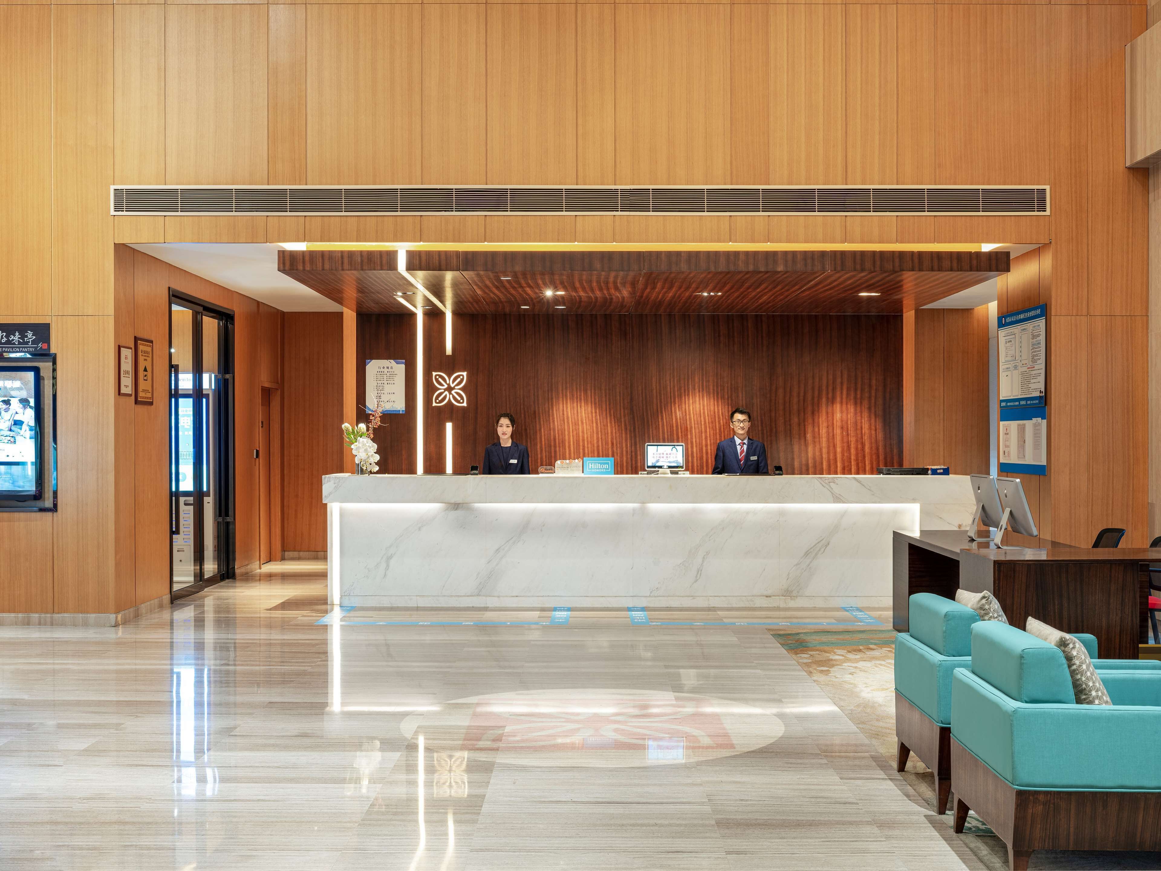 Zona de recepción de un hotel con mostrador de mármol, paneles de madera y un mostrador de atención al cliente.