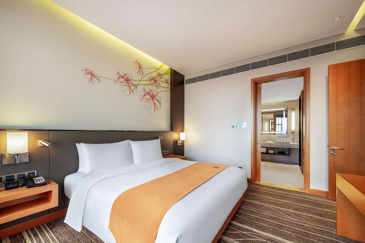 A hotel room with a large bed, bedside tables, a desk, and a bathroom visible through an open door.