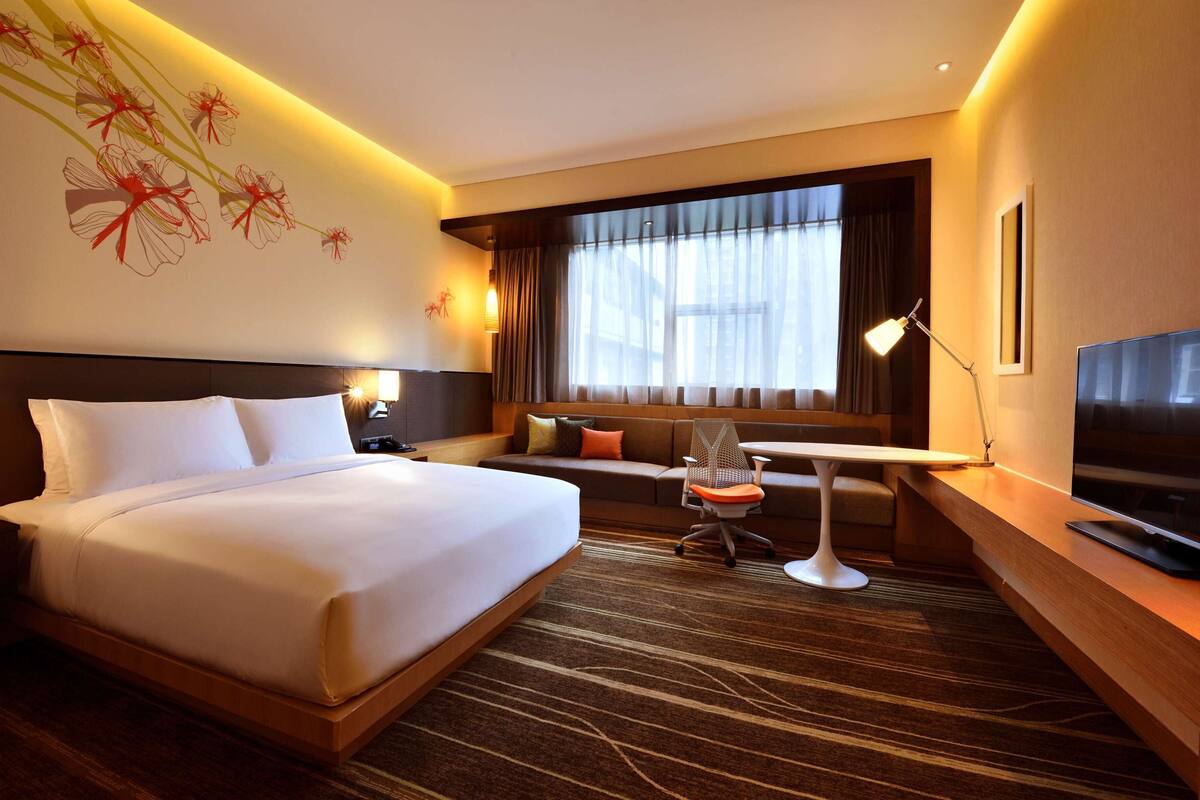 A hotel room with a large bed, a desk, a chair, a TV, and a window with curtains.