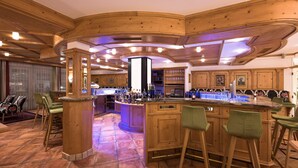 A bar area with wooden bar stools, a central bar counter, and a large illuminated column. - Hotel Seespitz (Ischgl)