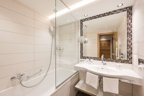 A modern bathroom with a glass-enclosed shower, a vanity with two sinks, and a large mirror with a mosaic border. - Hotel Seespitz (Ischgl)