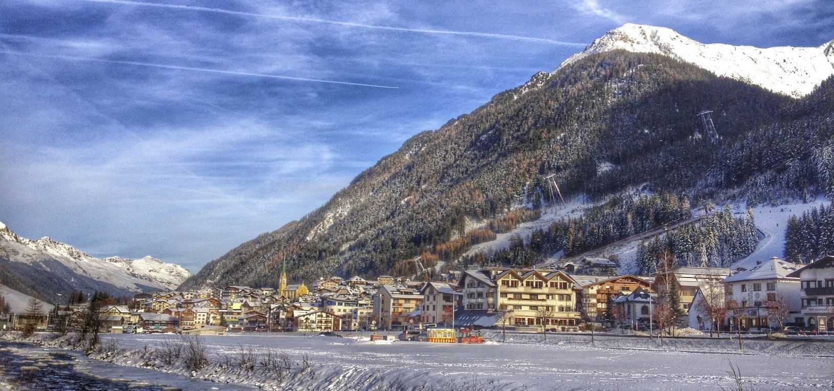A snow-covered mountain town with buildings along a river, surrounded by mountains.