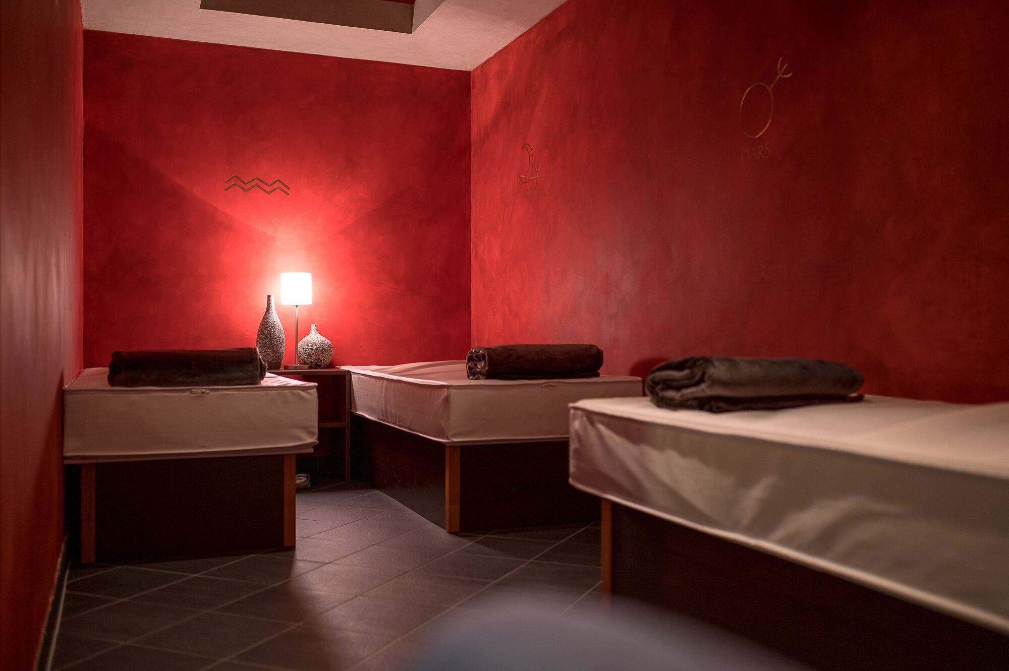 Una habitación con dos camas, una mesita de noche con lámpara, y una pared con el número 2 y un símbolo parecido al de género femenino.