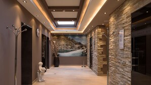 A modern hotel lobby with a stone wall, a large painting of a mountainous landscape, and a reception desk. - Hotel Seespitz (Ischgl)