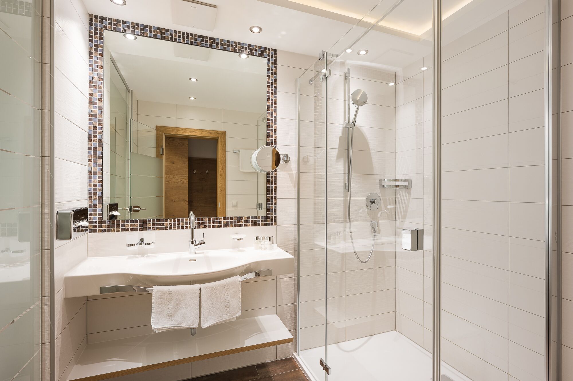 A modern bathroom with a glass-enclosed shower, a large mirror, and a vanity with two sinks.