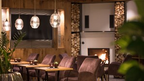 A cozy dining area with wooden walls, a fireplace, and hanging pendant lights. - Hotel Seespitz (Ischgl)