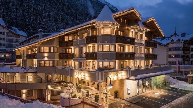 A multi-story hotel with balconies, a covered entrance, and a parking area. - Hotel Seespitz (Ischgl)