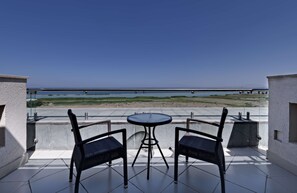 A balcony with two chairs and a table, overlooking a beach and a bridge. - DoubleTree by Hilton Hotel Van (Edremit)