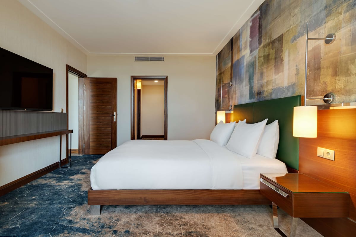 Habitación de hotel con una cama grande, televisión, cómoda de madera y un cuadro abstracto de colores.