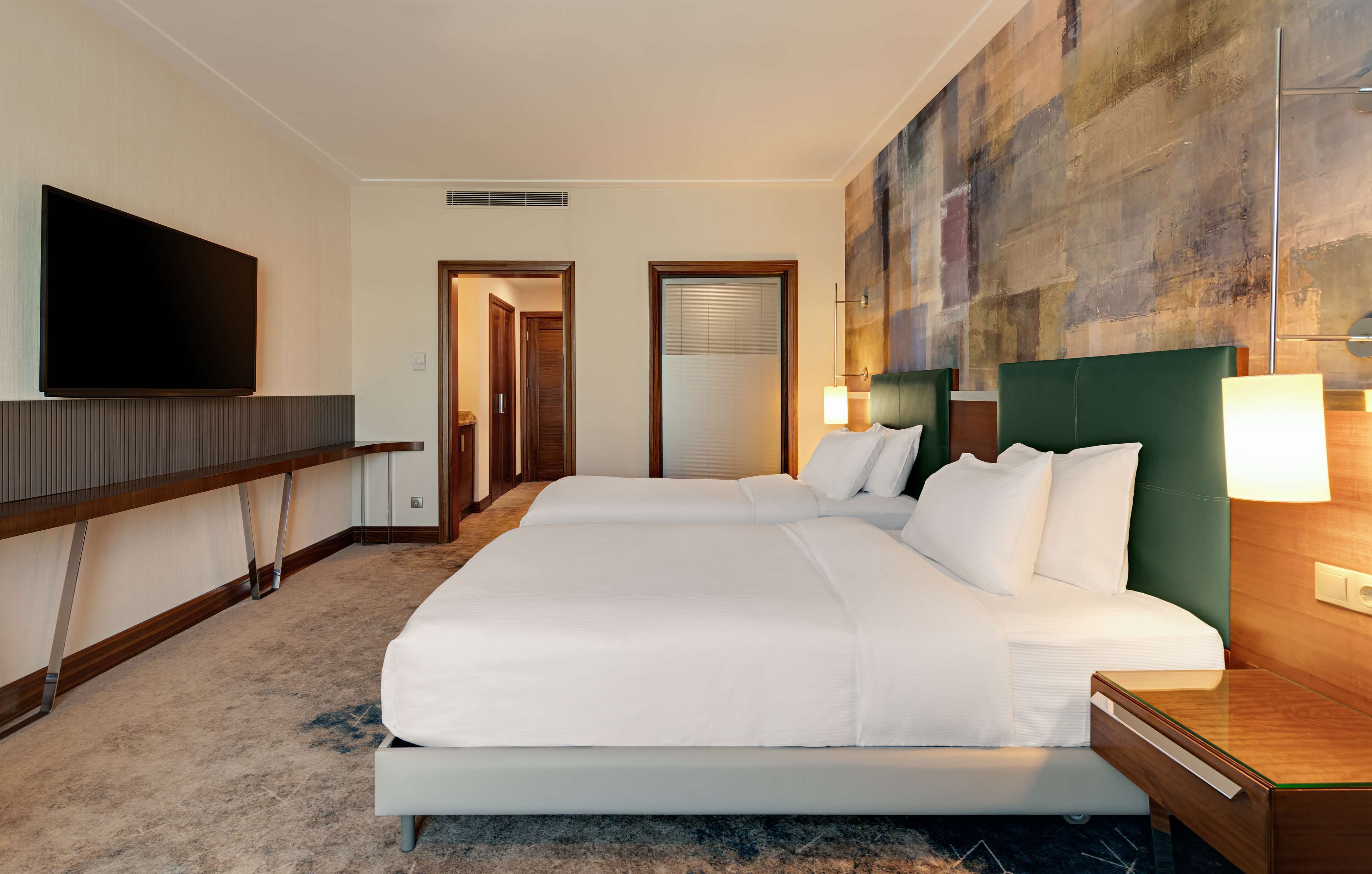 Habitación de hotel con dos camas, un televisor de pantalla plana, un cuadro abstracto grande y un escritorio de madera.