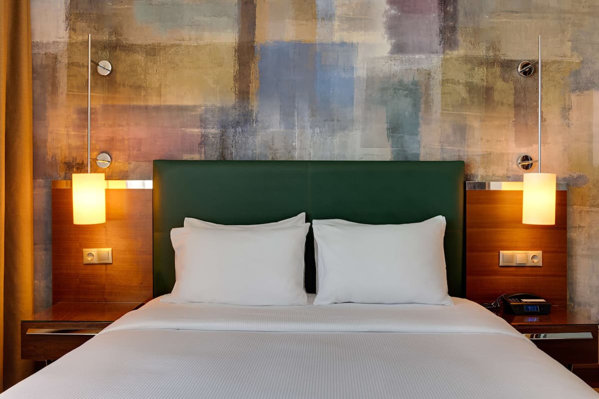 Habitación de hotel con una cama grande, dos mesitas de noche con lámparas y una pared texturizada detrás de la cama.