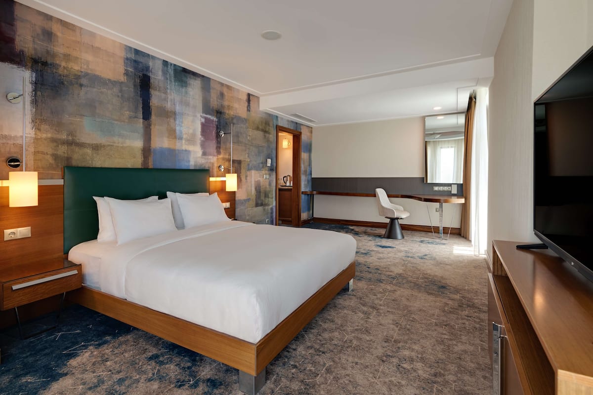 Habitación de hotel con una cama grande, un escritorio, una silla, un televisor y un baño visible a través de una puerta abierta.
