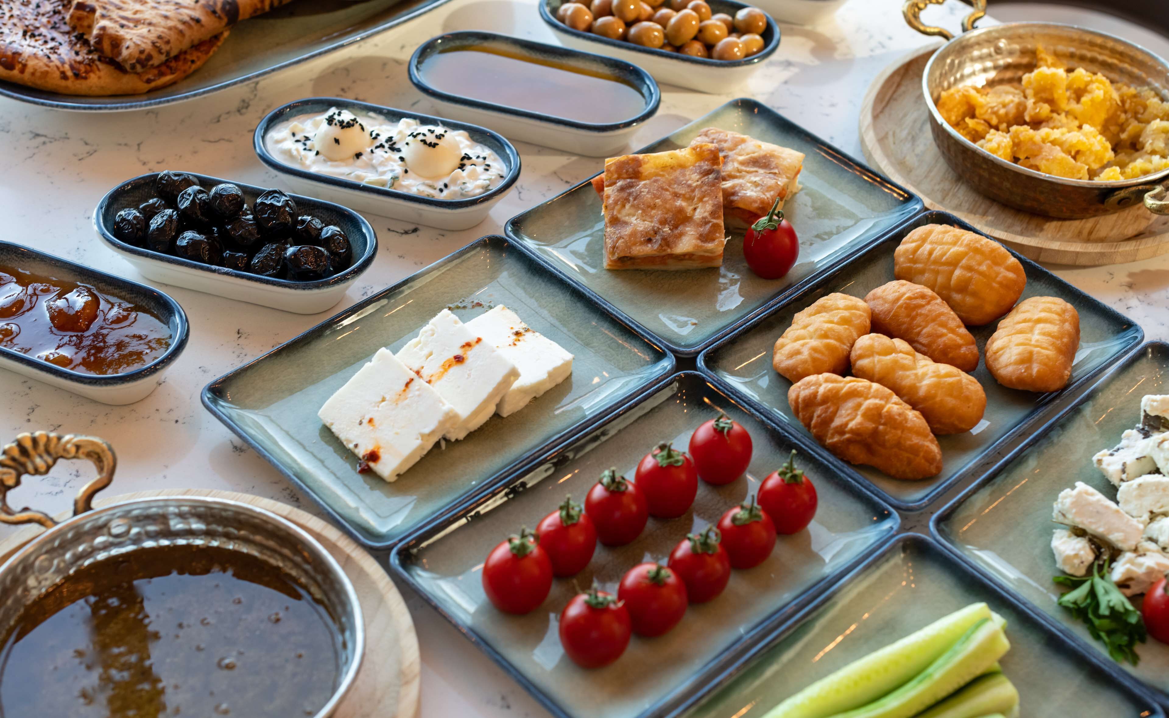 Variedad de alimentos sobre una mesa, como pasteles, queso y tomates.