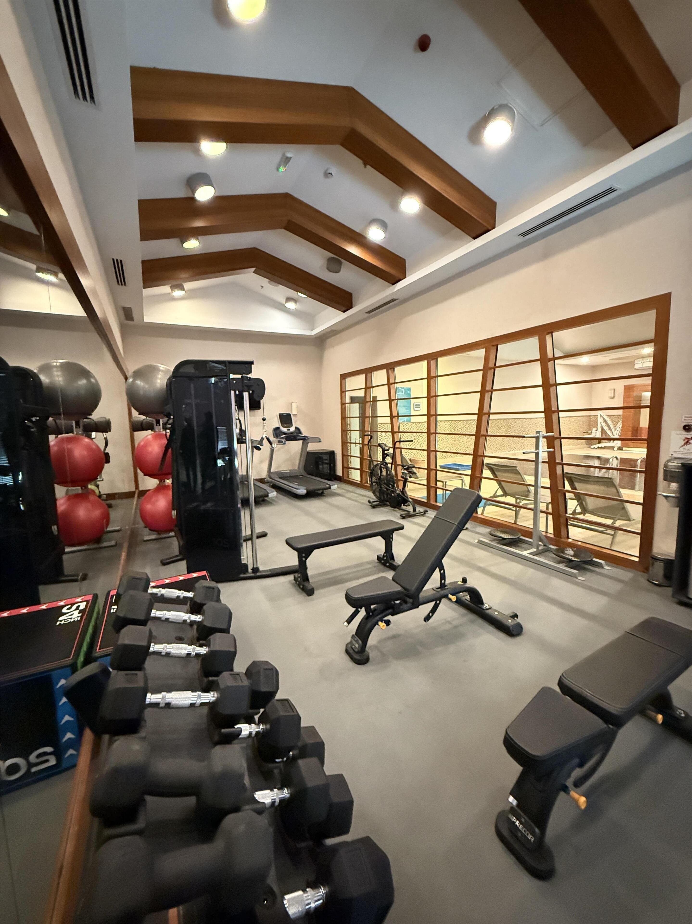 Ein Fitnessstudio mit Trainingsgeräten, Bänken und einer Spiegelwand.