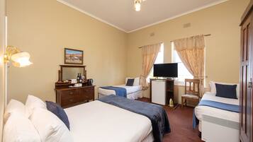 A hotel room with two beds, a desk with a computer, a television, and a ceiling fan.