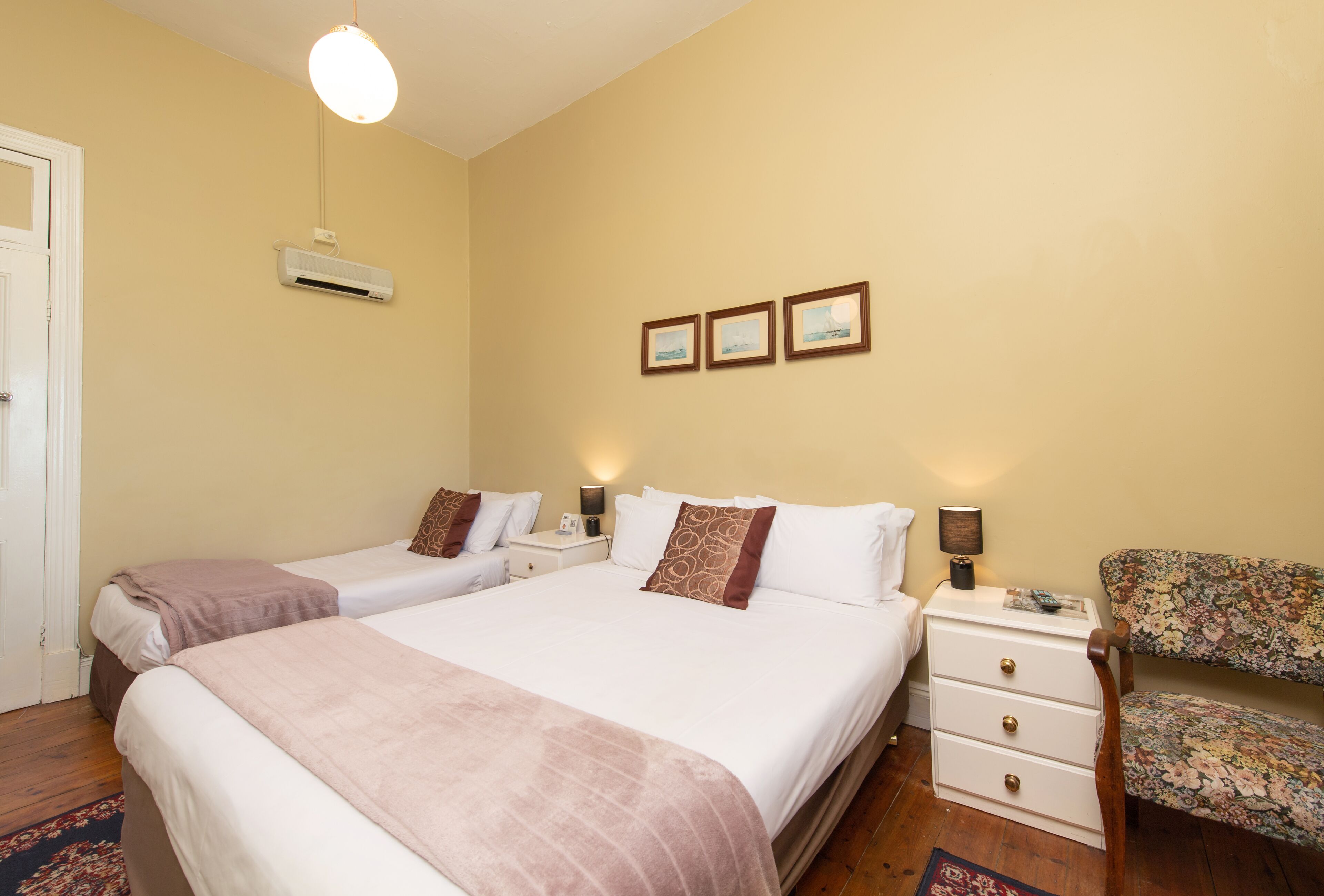 A bedroom with two beds, a nightstand, a chair, and a wall-mounted air conditioner.
