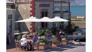 A coastal building with a sign reading "ANCHORAGE GUEST HOUSE" and outdoor seating with umbrellas.