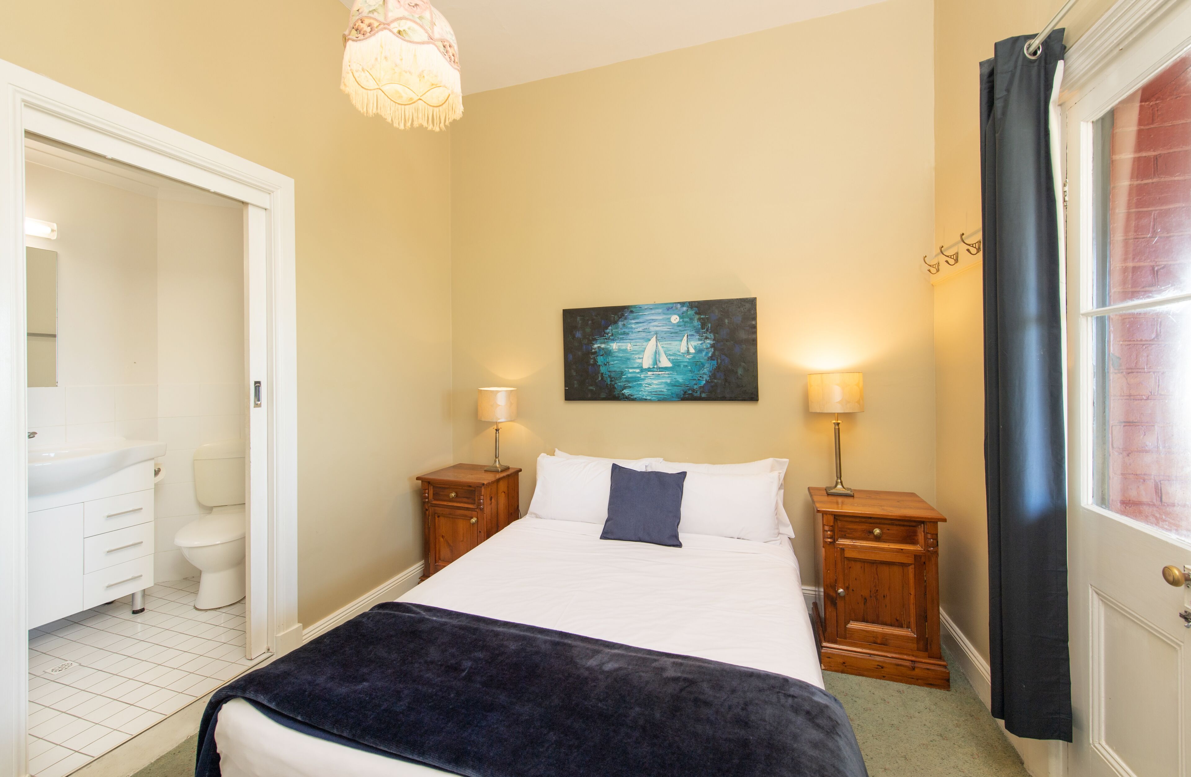 Een slaapkamer met een bed, nachtkastjes, een schilderij en een raam met gordijnen.