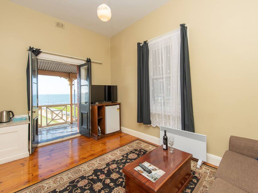 Una sala de estar con piso de madera, un sofá, una mesa de centro, un televisor y vista al mar a través de una puerta abierta.