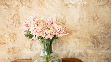 A clear glass vase with pink flowers on a wooden surface against a textured wall.