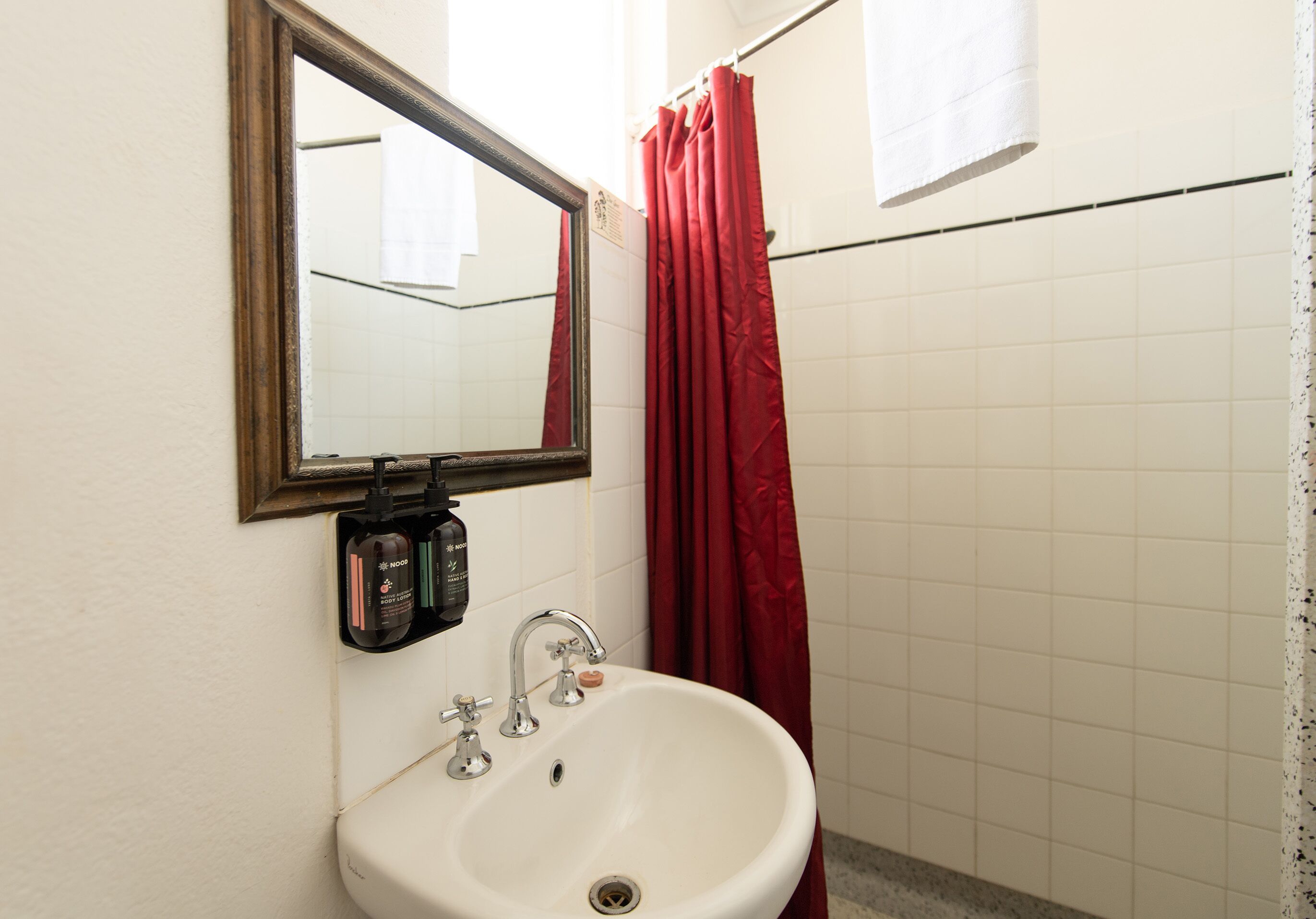 Un baño con lavamanos blanco, espejo y cortina de ducha roja.