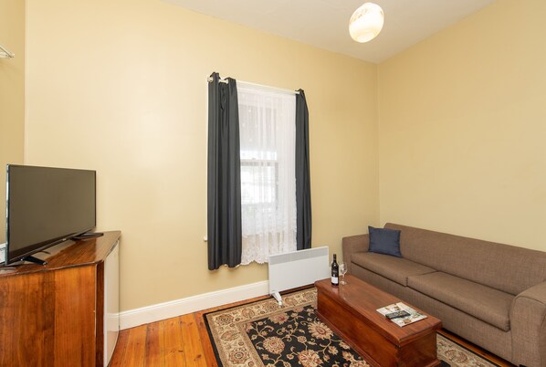 Una sala de estar con televisor sobre un mueble de madera, un sofá, una mesa de centro y un radiador.