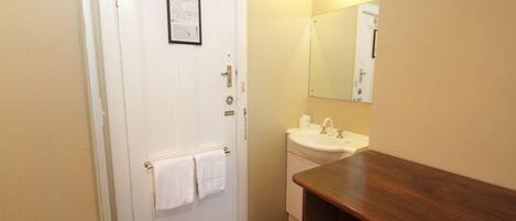 A bathroom with a white door, a sink, a mirror, and a wooden vanity.