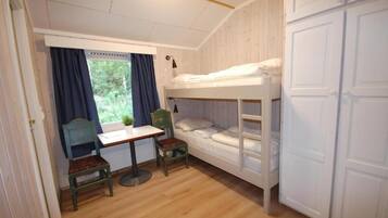 A small, cozy room with a bunk bed, a desk, two chairs, and a window with curtains.
