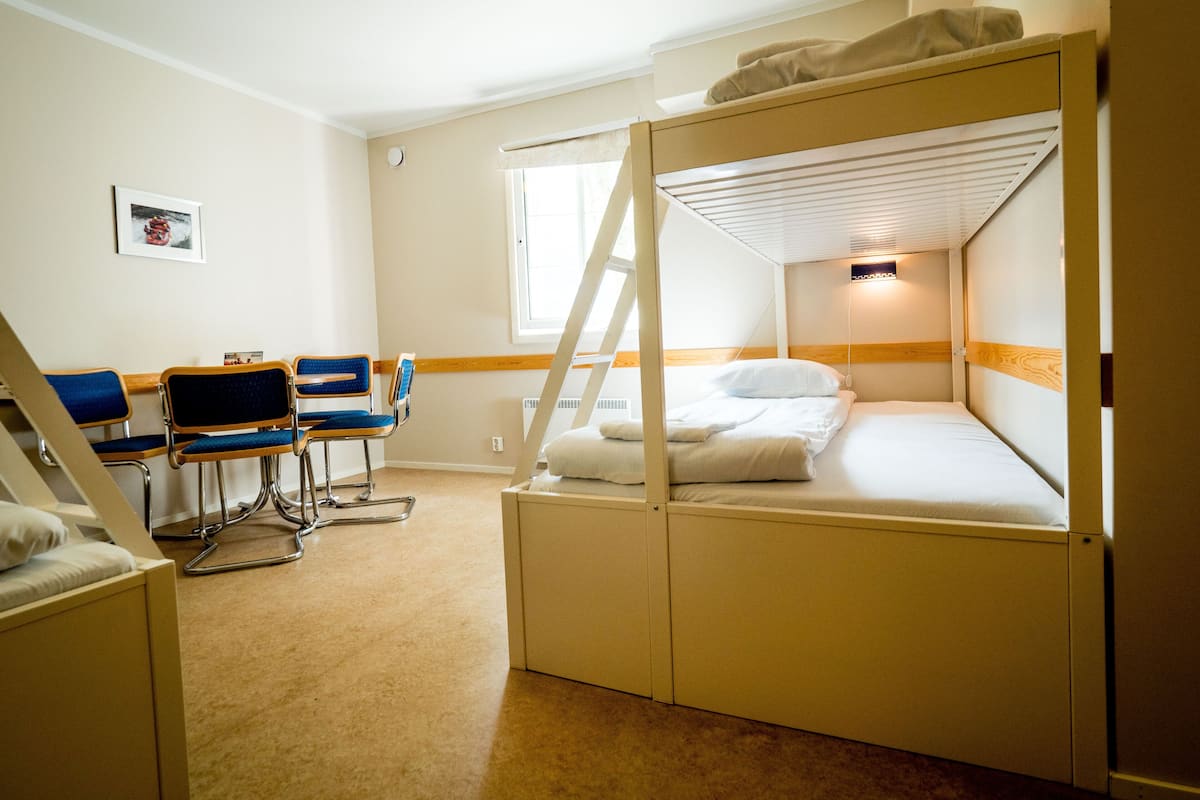 A bunk bed room with a desk and chairs, a window, and a picture on the wall.