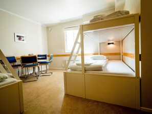 A bunk bed room with a desk and chairs, a window, and a picture on the wall.
