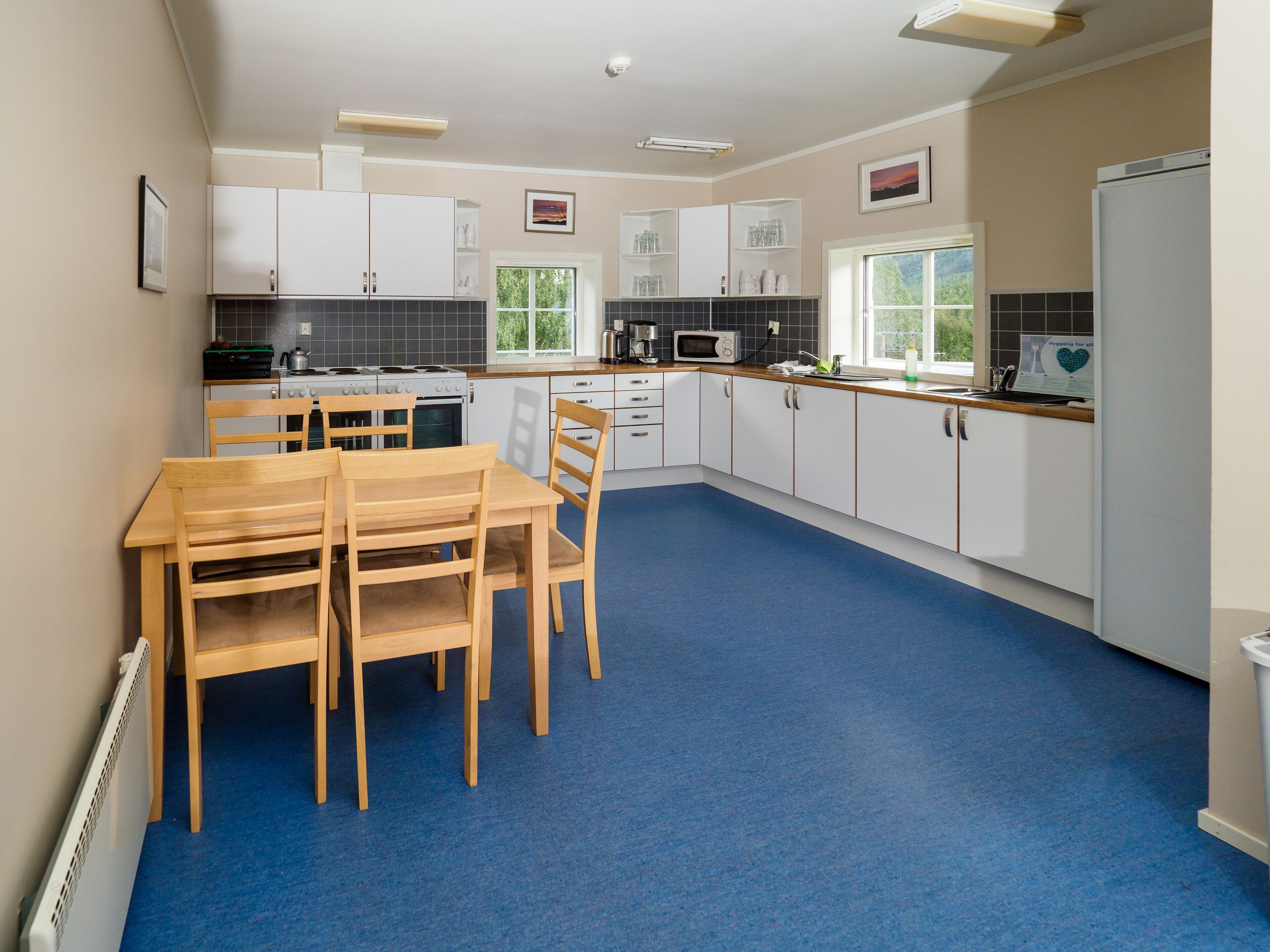 A modern kitchen with white cabinets, a dining table with chairs, and a blue carpet.