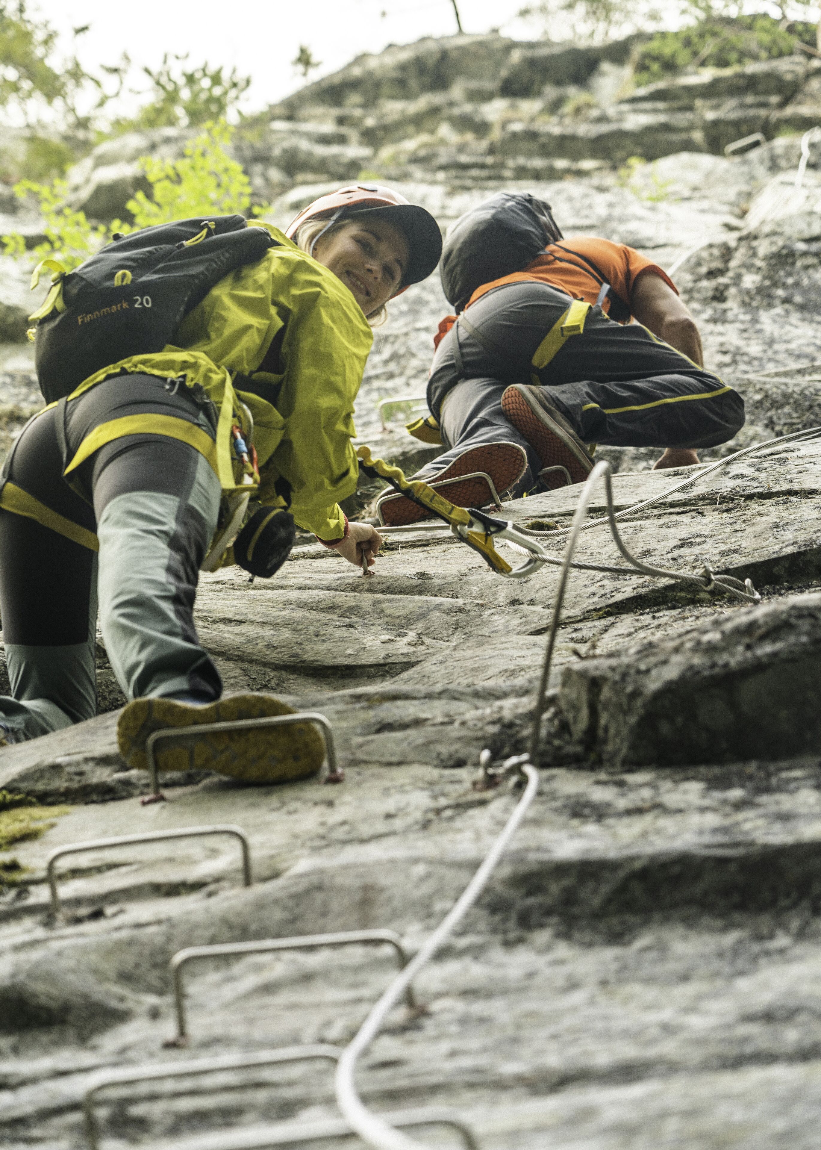 Two people climbing a rocky surface with climbing gear and ropes.