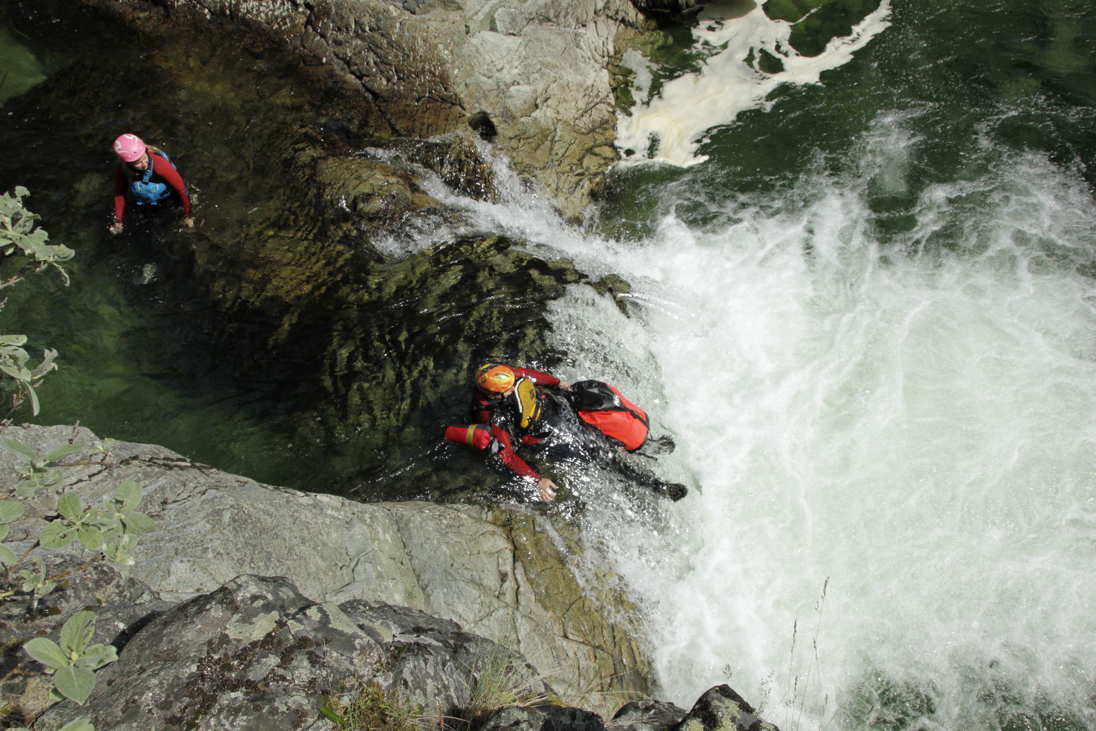 Una persona amb una jaqueta i casc vermells que s'obre pas per una cascada rocosa.